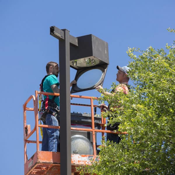 Electrical contractors removing an old HID lighting fixture from a shopping center parking lot pole.